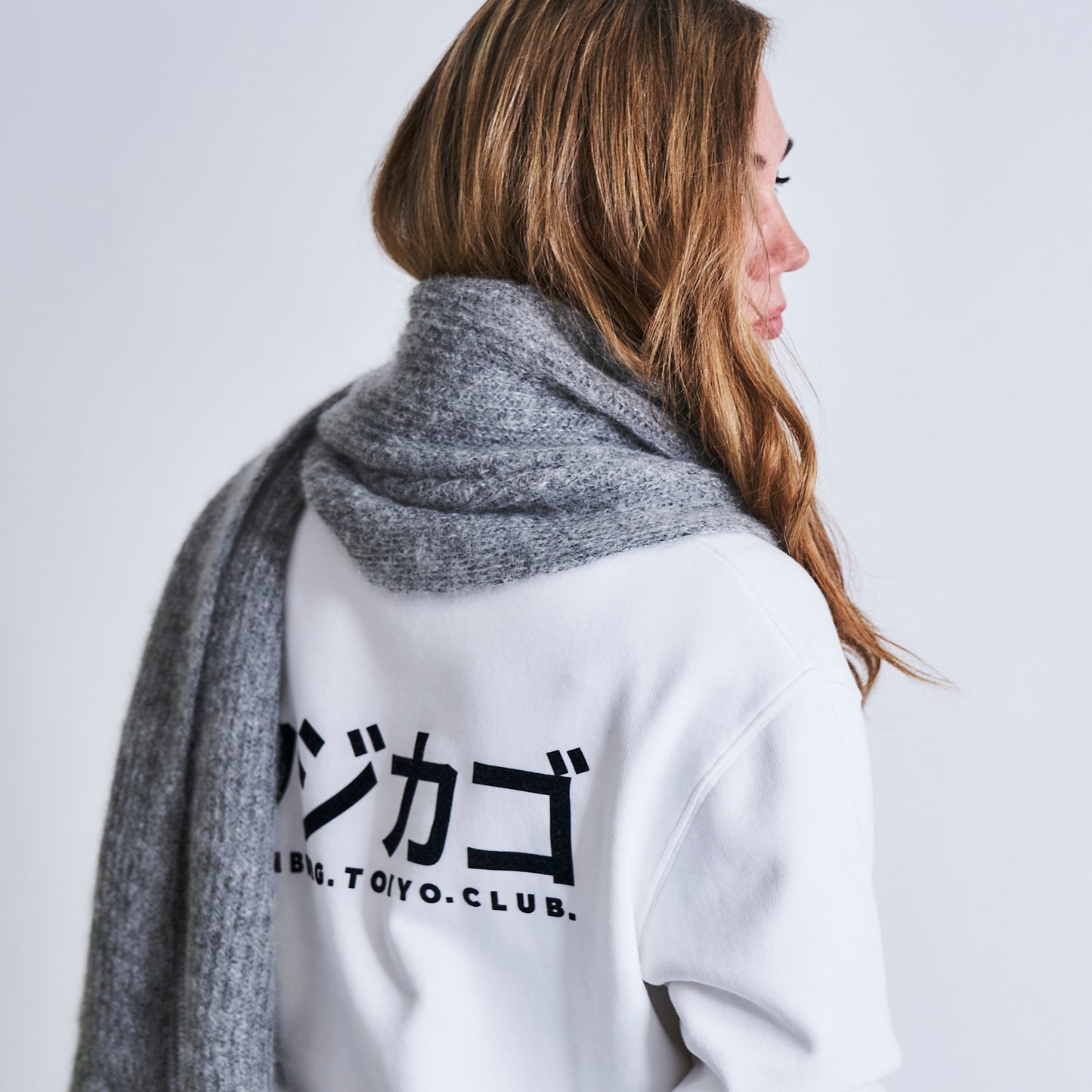 Frau mit grau meliertem Mohair Schal und weißem Fujicago Logo Pullover.