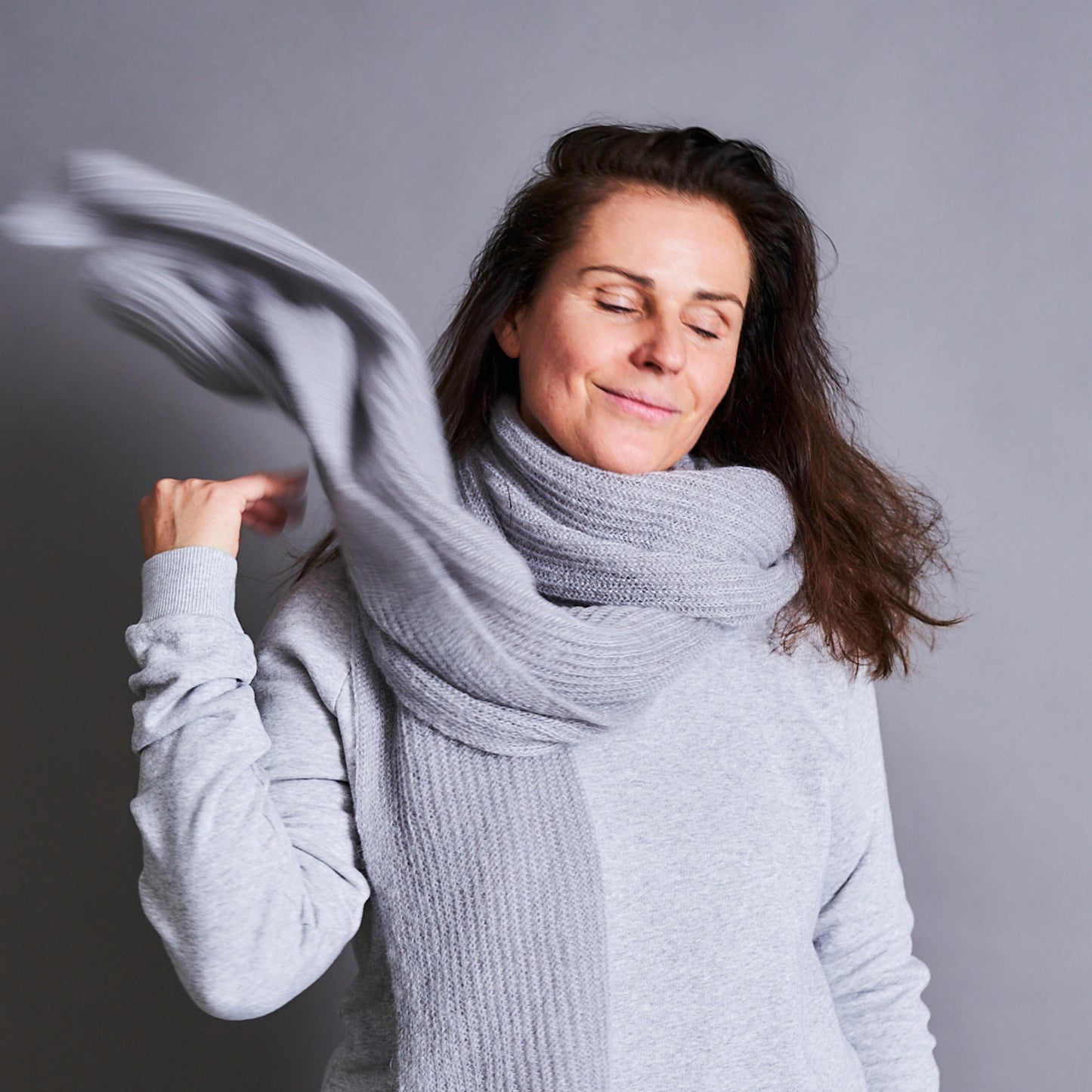 Eine Frau wirft sich einen hellgrauen Mohair Schal über die schulter.