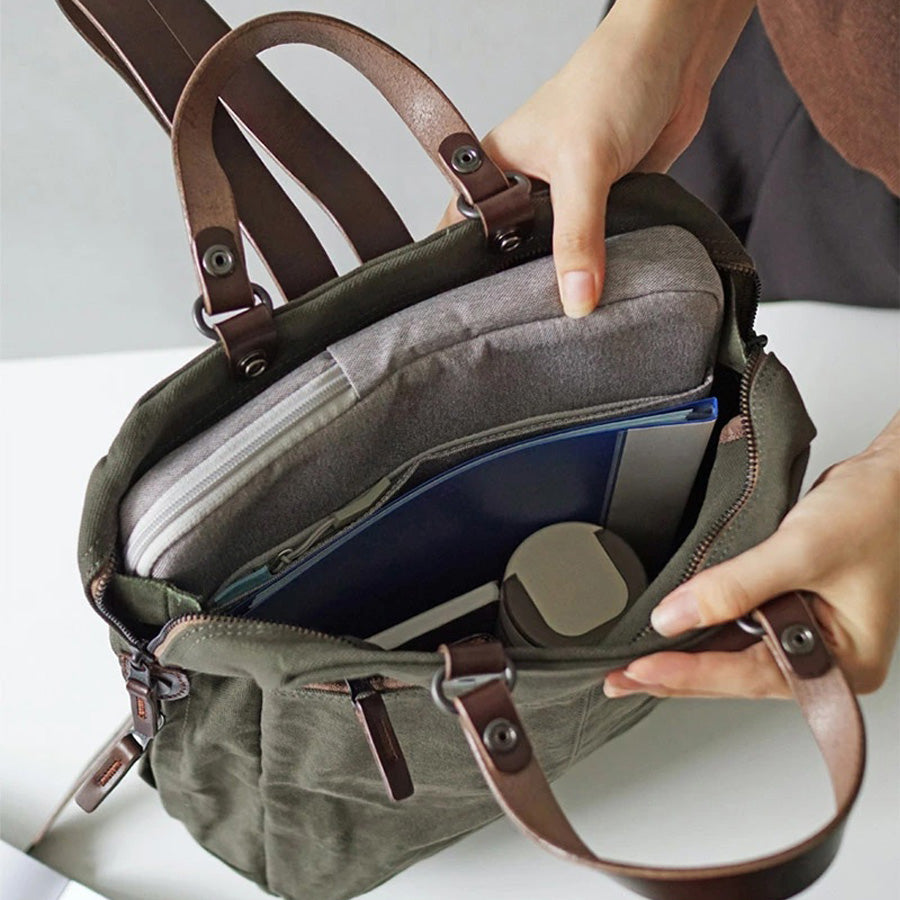 Person öffnet Khaki-grünen Rucksack mit braunen Lederschnallen von Baggyport aus Japan.